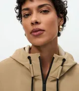 Campera cortavientos de color beige con diseño balonê, capucha con cordones ajustables, cierre frontal de cremallera y puños con elástico. Presenta un corte holgado y moderno.