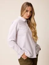 Camisa de manga larga con cuello clásico y cierre frontal de botones, confeccionada en tela de algodón con diseño de rayas verticales finas en color rosado y blanco. Presenta un bolsillo frontal en el pecho con detalle de etiqueta pequeña.