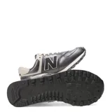 Championes urbanos New Balance modelo 574, color gris metalizado con detalles en crema y blanco. Presentan el logo N característico en los laterales, cordones al tono y suela con tecnología de amortiguación.