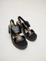 Sandalias negras de cuero con plataforma y taco cuadrado. Tienen dos tiras anchas sobre el empeine, correa trasera con elástico y argollas metálicas decorativas en los laterales.