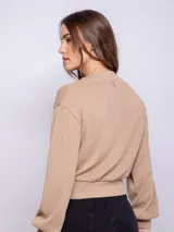 Cárdigan corto color beige, de manga larga y escote en V. Tiene cuatro botones brillantes.