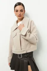 Tapado corto color beige, de cuello grande, con dos bolsillos de solapa y mangas con dobladillo y aro metálico.