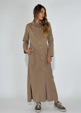 Vestido largo tipo camisero color beige, con cuello clásico, botones frontales de arriba a abajo, mangas largas con puños abotonados, dos bolsillos con solapa en el pecho y aberturas laterales en el ruedo.