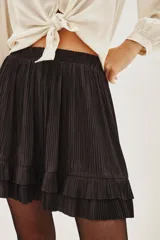Falda corta de color negro con diseño plisado y detalle de volado en el ruedo. Presenta una cintura ancha con apliques de tachas metálicas decorativas.