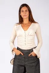 Body de velour color beige, con escote en V, mangas largas acampanadas y frente fruncido con cierre de botones decorativos.