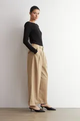 Pantalón pinzado de corte ancho, color beige, con bolsillos laterales y botamanga con vuelta.