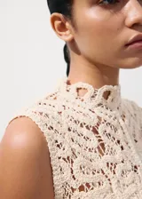 Top de tejido calado color beige, con cuello halter, sin mangas y cierre de botones en la espalda.