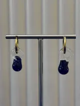 Aros tipo argolla dorada con dije colgante de vidrio soplado en forma de lágrima, combinando una parte transparente con una base en color azul intenso.