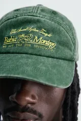 Gorra de siete paneles verde oscuro con efecto lavado, visera curva y bordado frontal en tono amarillo con la inscripción 'Bahia Montego'. Cuenta con ajuste posterior.