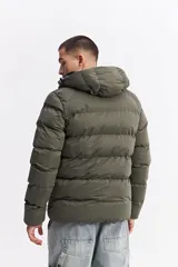 Campera puffer con capucha, diseño acolchado, cierre frontal y bolsillos laterales. Presenta un interior en contraste de color verde oliva.