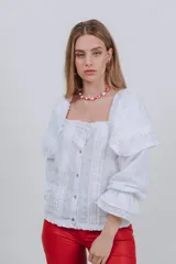 Blusa blanca con bordado inglés, escote cuadrado, mangas largas abullonadas con volados y cierre frontal con botones.