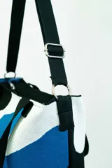 Bolso tipo tote con estampado abstracto en tonos azul, blanco, negro y verde. Tiene doble asa de mano y correa larga regulable al hombro, ambas en color negro.
