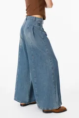 Jean de corte wide leg con pinzas frontales y costuras verticales decorativas. Presenta un diseño de tiro alto con cierre de botón y cremallera, confeccionado en denim de lavado medio.