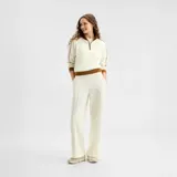 Pantalón deportivo New Balance Sport Legacy, de color blanco crudo, con diseño de pierna recta, bolsillos laterales y líneas con costuras frontales.