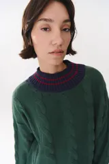 Buzo de tejido de punto con diseño de trenzas, color crema con detalles en marrón en cuello, puños y ruedo. Presenta líneas finas en contraste y pequeñas costuras decorativas en forma de cruz.