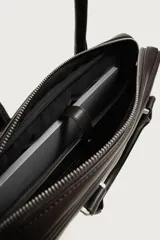 Maletín slim de textura grabada color marrón, con compartimento principal con cierre de cremallera, bolsillo interior para dispositivos electrónicos de hasta 13 pulgadas y bolsillo frontal con cierre. Incluye dos asas de mano y un asa de hombro ajustable y extraíble.