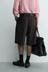 Bermuda negra de corte ancho (wide fit) confeccionada en tejido con mezcla de viscosa. Presenta pliegues en el delantero, bolsillos frontales y bolsillos de vivo en la parte trasera. Cierre frontal con cremallera y gancho metálico oculto.