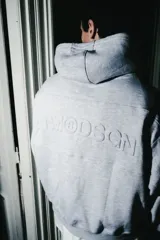 Hoodie de algodón color gris melange, con capucha ajustable mediante cordones, bolsillo frontal tipo canguro y logo bordado en relieve en el pecho.
