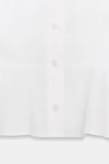 Camisa lisa de algodón blanco, con cuello solapa, manga corta abullonada y bajo en evasé con detalle de peplum. Cierre frontal con botones.