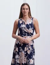 Vestido largo de seda fría con estampado floral en tonos beige y blanco sobre fondo azul marino. Tiene cuello redondo cruzado con abertura y aplique metálico.