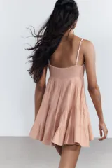 Vestido corto negro de gasa con escote recto y tirantes finos ajustables. El corpiño tiene fruncido elástico y el ruedo es escalonado con volados. Presenta un detalle de encaje a tono en el borde del escote.