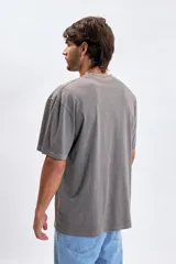 Remera de manga corta con efecto lavado, color gris oscuro, con cuello redondo y un pequeño parche rectangular con texto en el pecho.