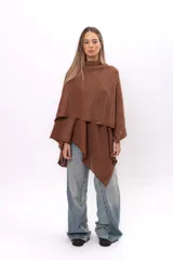 Ruana tejida de punto con cuello alto, confeccionada en una mezcla de algodón y lurex que le otorga un acabado brillante. Presenta un diseño asimétrico con caída fluida y holgada.