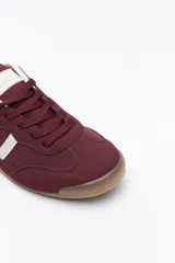 Zapatilla urbana de perfil bajo con diseño retro, confeccionada en poliuretano con detalles en textura tipo gamuza. Presenta puntera redondeada, cordones clásicos y suela de goma color caramelo.