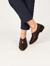 Mocasines de charol color bordó, de diseño vanguardista con corte asimétrico en el empeine, abertura en V, punta fina y suela plana con pequeño tacón.