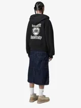 Campera con capucha Carhartt, color negro, con cierre frontal completo y logo bordado en tipografía gótica en el pecho. Cuenta con bolsillos tipo canguro y puños y ruedo acanalados.