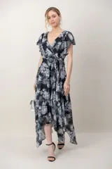 Vestido midi de gasa estampada con flores en tonos negro, gris y blanco, con destellos de hilos de plata. Presenta escote cruzado en V, mangas cortas acampanadas, lazo ajustable en la cintura y falda de corte asimétrico.