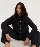 Camisa de jean negra con abotonado delantero, cuello solapa, mangas largas, recortes y bolsillos grandes en el pecho.