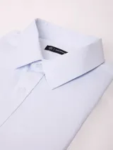 Camisa de vestir de manga larga en color celeste claro, con cuello clásico y cierre frontal de botones. Presenta un diseño de textura sutil y corte regular.