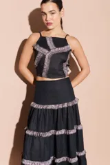 Top corto color turquesa con tirantes finos y detalles de volantes brillantes en color beige que forman un patrón geométrico en el frente.