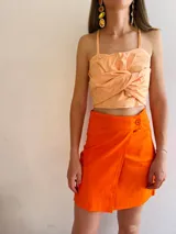 Minifalda cruzada color naranja de lino con un botón a la vista.