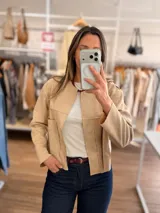 Chaqueta corta de textura efecto ante en color beige, con diseño abierto, cuello redondo y bolsillos frontales. Presenta costuras horizontales decorativas y mangas largas.