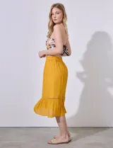 Falda midi color mostaza, de gasa bambula con pretina smock, lazo de ajuste, volado en el ruedo y aplique de puntilla.