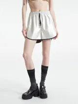 Short plateado de cuerina, con cintura elástica y cordón ajustable. Presenta vivos negros en el ruedo.