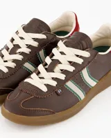Championes Coolway modelo Kiro Espresso Pace de estilo retro, fabricados principalmente en gamuza color marrón. Presentan doble franja lateral en color blanco con bordes verdes, cordones claros, detalle rojo en la parte trasera del talón y suela de goma translúcida.