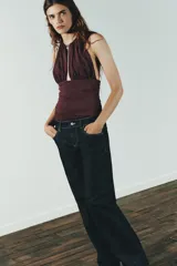 Body color borgoña de cuello halter con escote pronunciado, detalle de pieza metálica y aplicación joya. Tejido drapeado y cierre inferior con botones a presión y en cuello con gancho metálico.