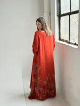 Vestido largo color terracota con escote en V, mangas tres cuartos y diseño amplio, decorado con un estampado floral grande en tono marrón en la parte inferior.