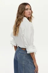 Camisa blanca de manga larga abullonada con detalle de punto smock en los puños y cordones para atar. Presenta cuello clásico y cierre frontal de botones.