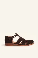 Sandalias de gamuza color marrón, estilo romano con diseño en T, tiras con aberturas laterales y cierre de hebilla metálica en el tobillo. Cuenta con tacón bajo de madera.