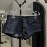 Short de denim azul oscuro, de tiro bajo, con bolsillos delanteros y traseros, costuras pespuntadas en tono contrastante y cierre frontal con botón y cremallera.