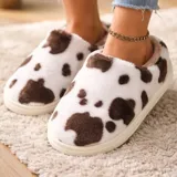 Pantuflas sin talón confeccionadas en algodón afelpado y piel sintética, con divertido estampado de manchas de vaca en tonos blanco y marrón, y suela de PVC.