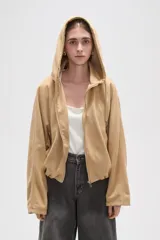 Campera de suede color beige con capucha, cierre frontal completo y mangas largas. Presenta un diseño holgado con bolsillos laterales y detalles de frunces en el ruedo.