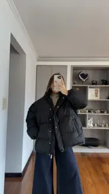 Campera puffer negra de corte oversize, con cuello alto, cierre frontal y botones a presión. Cuenta con mangas largas con puños elásticos y diseño acolchado.