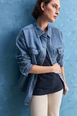 Sobrecamisa de denim de calce amplio y color azul, con cuello clásico, cierre frontal con broches metálicos y bolsillos delanteros con solapa.