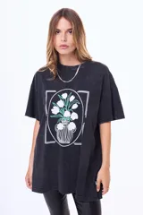 Remera de algodón con efecto acid wash en color negro, de corte oversize y manga corta. Presenta un estampado frontal enmarcado que ilustra un jarrón con flores blancas.