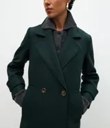 Abrigo largo de paño color verde oscuro, con solapas amplias tipo blazer, cierre frontal cruzado con botones y abertura trasera. Diseño estructurado y elegante.
